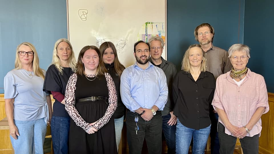 Nio personer står i en grupp och tittar in i kameran.