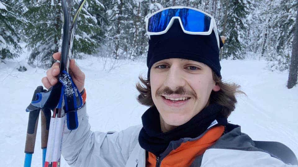En man står i ett skidspår. Han håller ett par skidor i ena handen. 