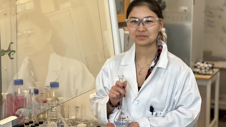 En kvinna i vit rock och skyddsglasögon står i ett laboratorium.