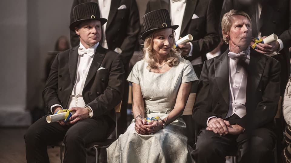Finklädda personer med lagerkransar och doktorshattar på en scen. 
