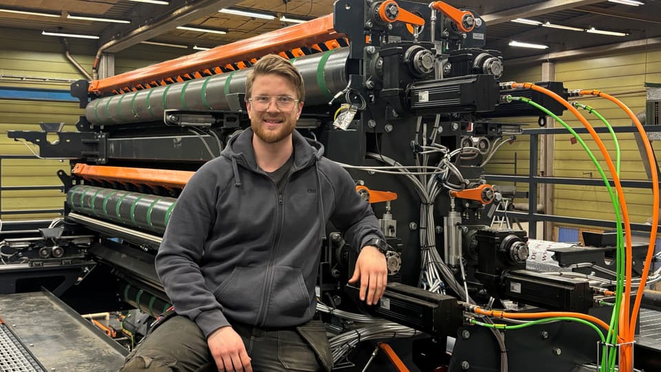En man sitter framför en industrimaskin.