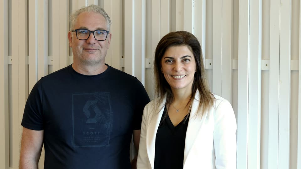 Professor Mikael Gidlund och Professor Sinem Coleri står tillsammans framför en ljus trävägg under hennes besök vid Mittuniversitetet.