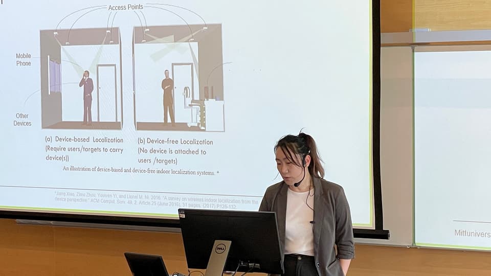 En kvinna med mörkt hår uppsatt i en hästsvans står vid en dator och håller en presentation.