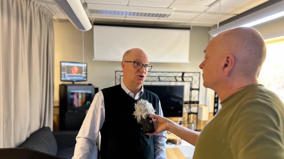 A man with a green shirt is interviewing a man with a navy shirt