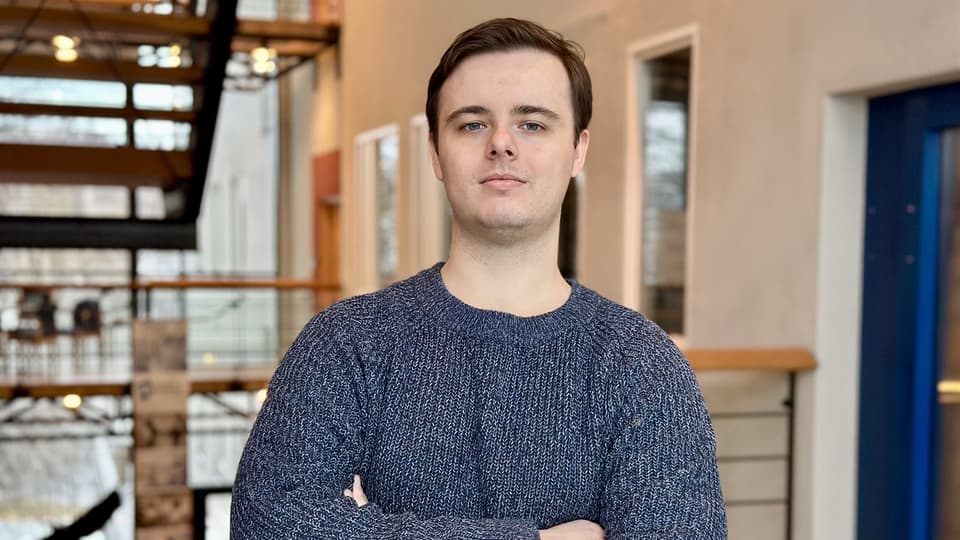 Ung man med brunt hår och mörkblå tröja.