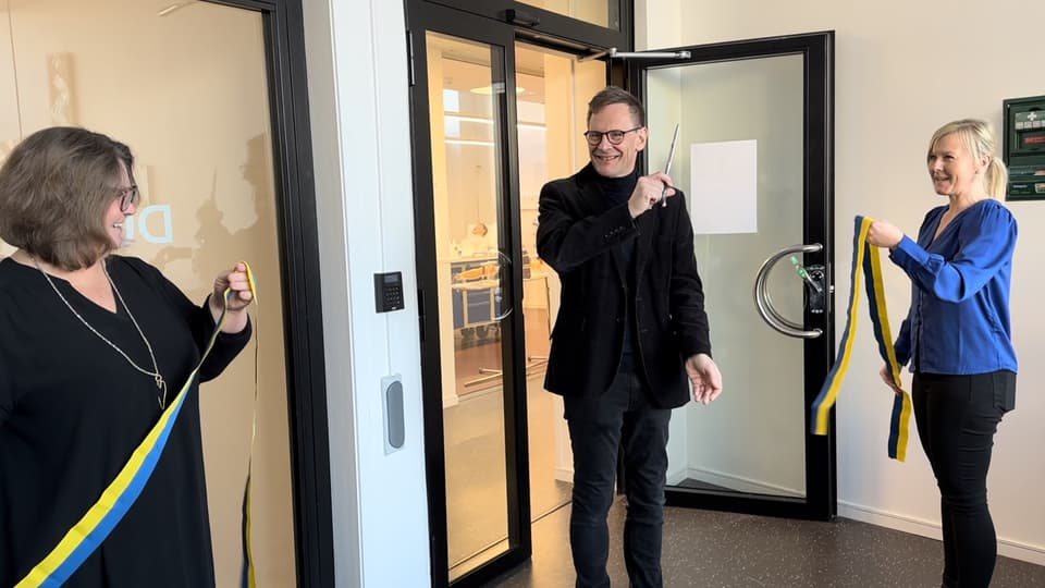 Två personer håller i ett gulblått band som den tredje personen nyss har klippt av.