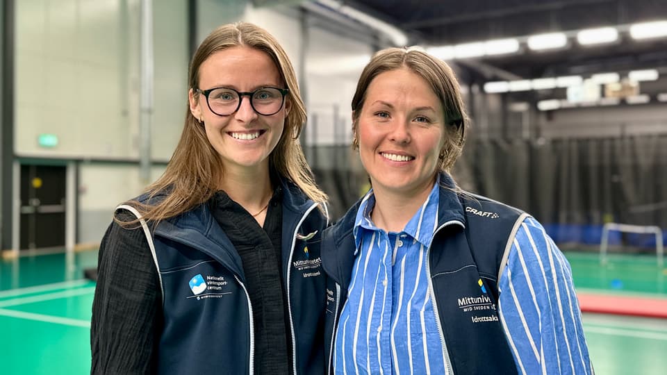 Två kvinnor står bredvid varandra i en sporthall. De ler mot kameran.