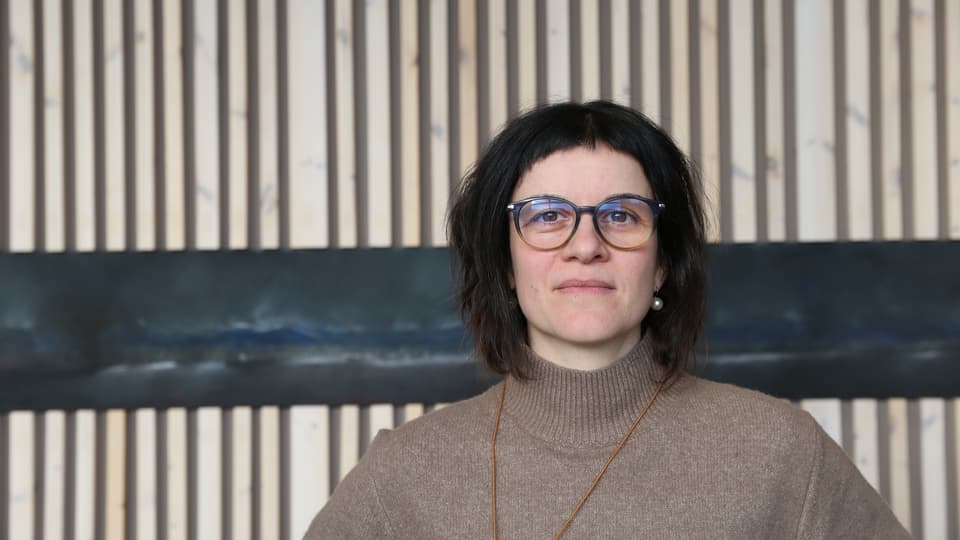 Allvarlig kvinna med glasögon framför träpanel.