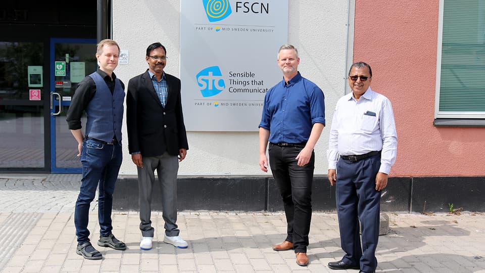 Fyra män som står vid en fasadskylt med texten STC Research Center.