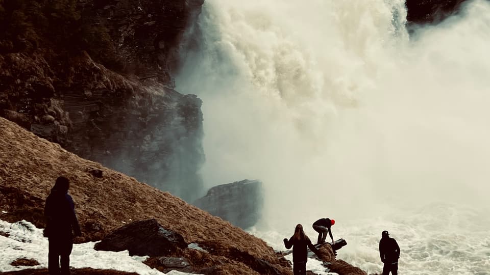 Three black siluettes standing in front of a huge waterfall