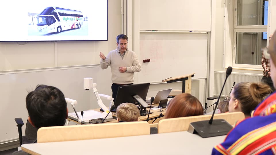 En man i ljus tröja står och presenterar för en publik