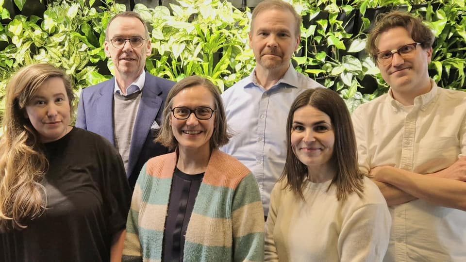 Tre män och tre kvinnor står i grupp framför gröna buskar.