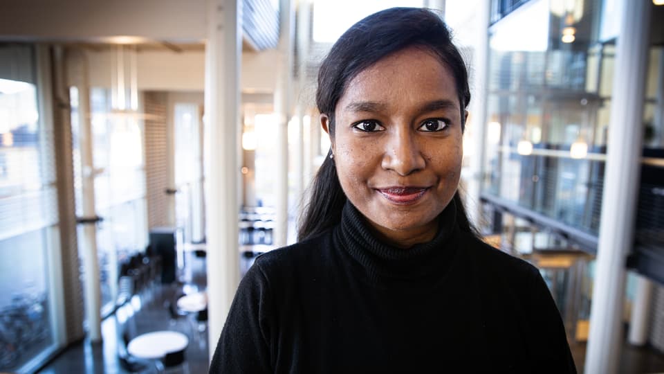 Kvinna med svart tröja och svart hår tittar in i kameran.