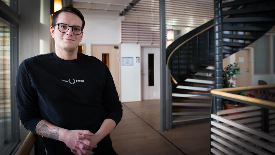 En man med svarta glasögon och svart tröja står vid ett trappräcke.