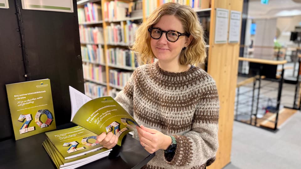 Person som står och bläddrar i den gröna jubileumsboken.