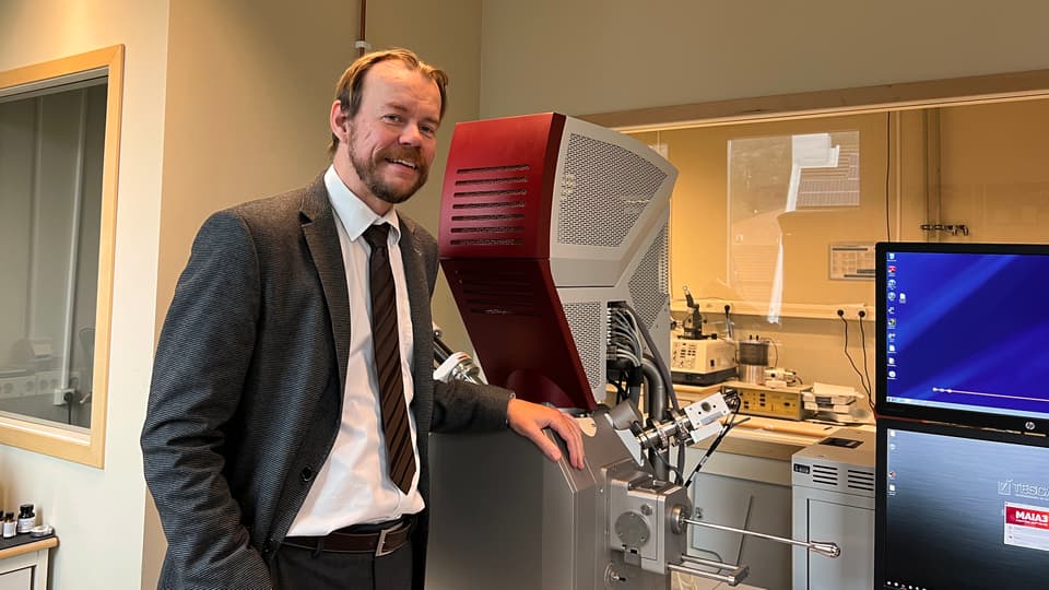 En man står framför laboratorieutrustning och bildskärmar.