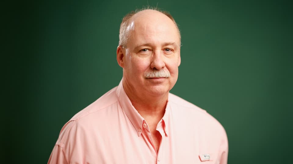  A man in a pink shirt looks into the camera.