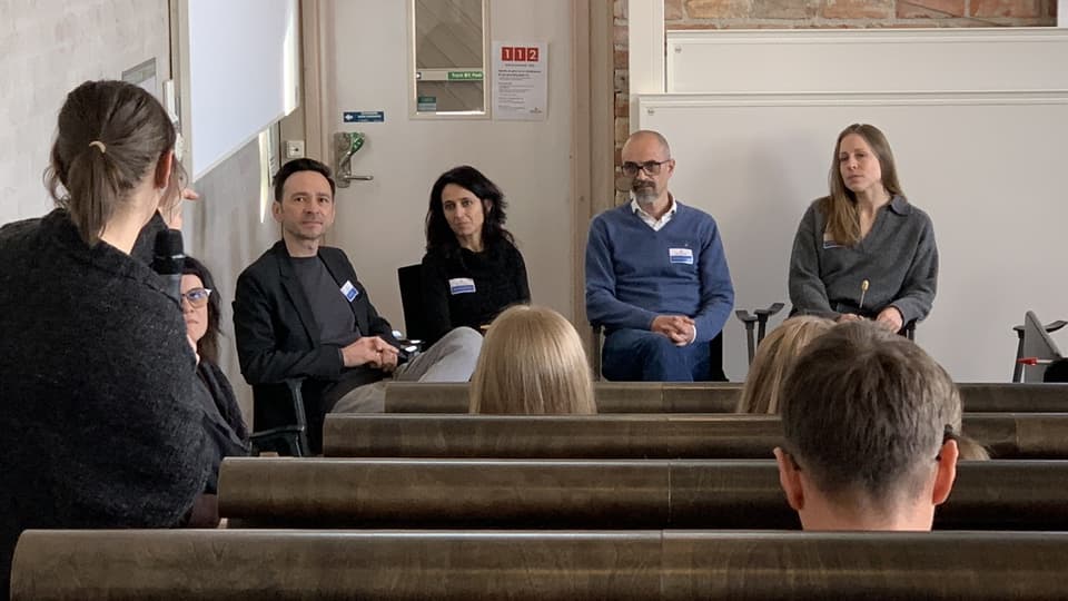 En panel med fyra personer sitter längst fram i en föreläsningssal med publik.