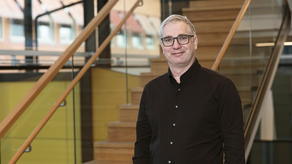 Man med glasögon i svart skjorta framför en trappa