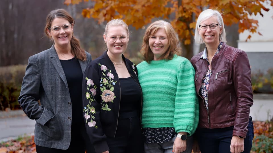 Gruppbild på fyra leende kvinnor framför träd