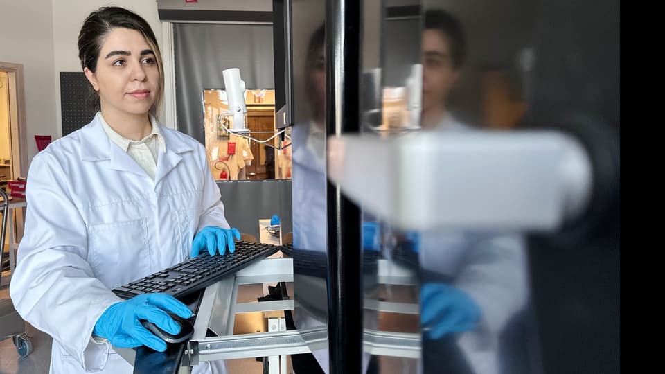 En kvinna i vit labbrock och blå handskar i labbet.