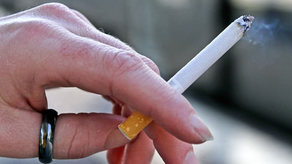 Hand som håller i en tänd cigarett.