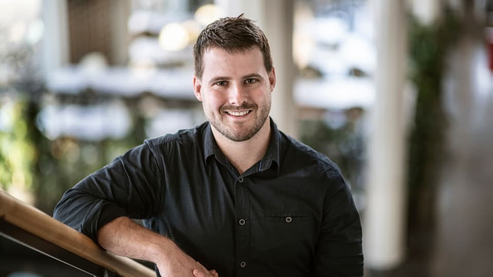 Daryl Aubry, doktorand, står i en trappa på Campus Östersund. Han är glad. 