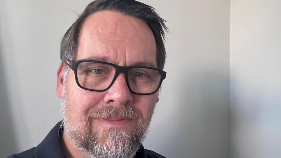 Porträttfoto av en man med brunt hår och mörka glasögon