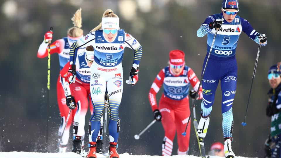 Fyra längdskidåkare i tävlingsdräkter i snöiga skidspår.
