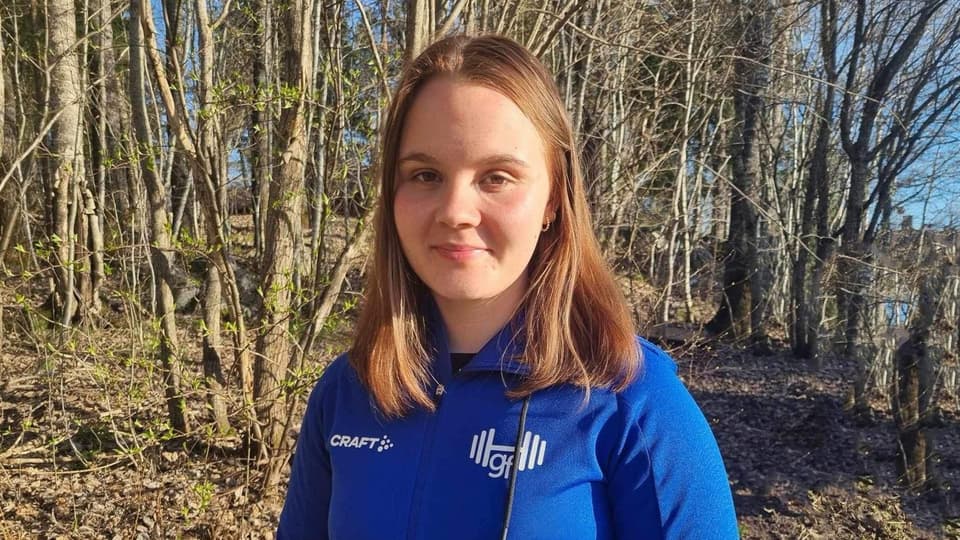 Porträttbild utomhus. En ung tjej med blont hår och i blå tröja står framför en skogsdunge