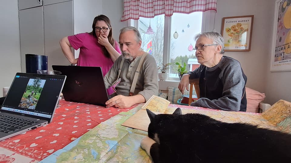 Tre personer arbetar vid ett köksbord. En katt ligger på en karta.