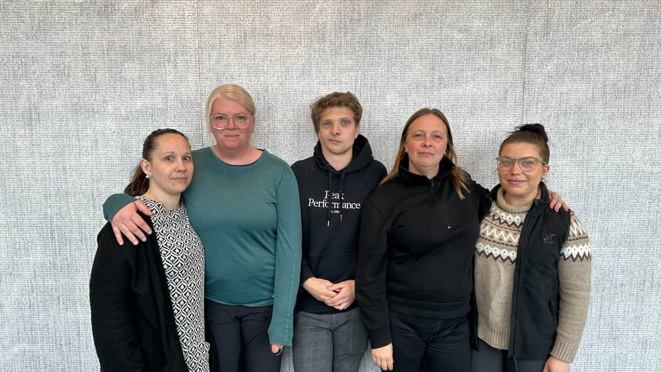 Fyra kvinnor och en man fotograferade framför en grå bakgrnd