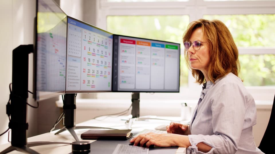 Kvinna som sitter och jobbar framför datorskärmar
