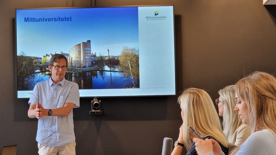 Man framför en skärm presenterar för sittande publik.