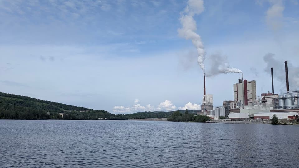 Fabrik med bolmande rök invid vatten