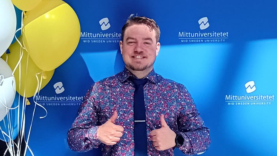 En man står framför en blå bakgrund, men några ballonger vid sidan om.