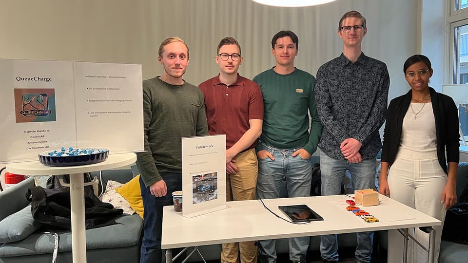 Fem personer står bakom ett bord där en prototyp på ett virtuellt kösystem för elbilsladdare ligger.