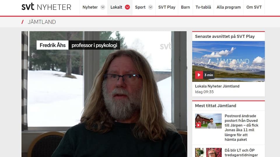 Skärmklipp från nyhetssida med en bild av en skäggig man framför ett fönster.