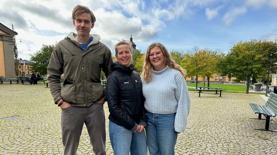 Tre personer stående på ett torg.