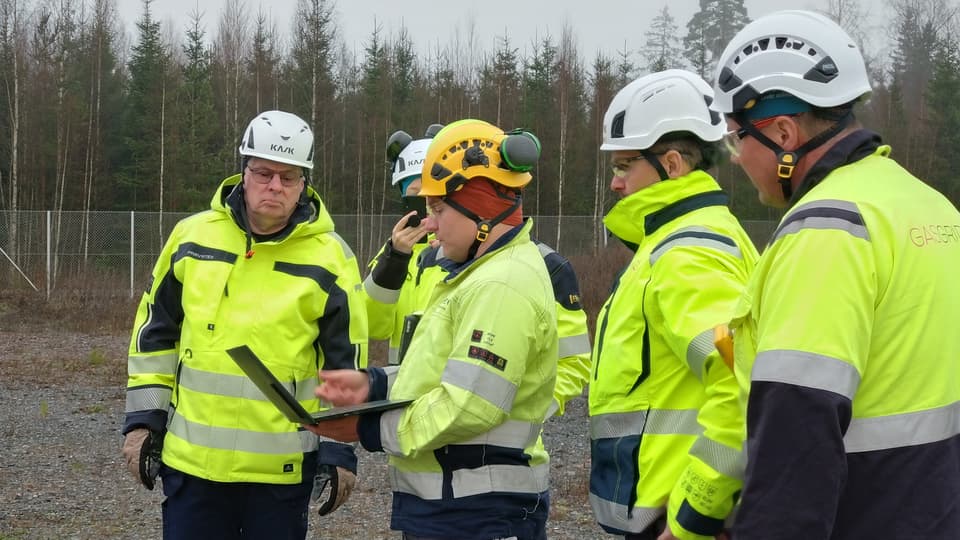 En grupp män i varselkläder står tillsammans och tittar på en bärbar dator. 