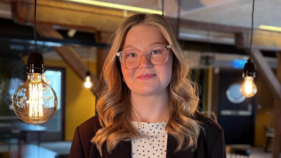 En kvinna ser in i kameran och ler. Lampor hänger i bakgrunden.