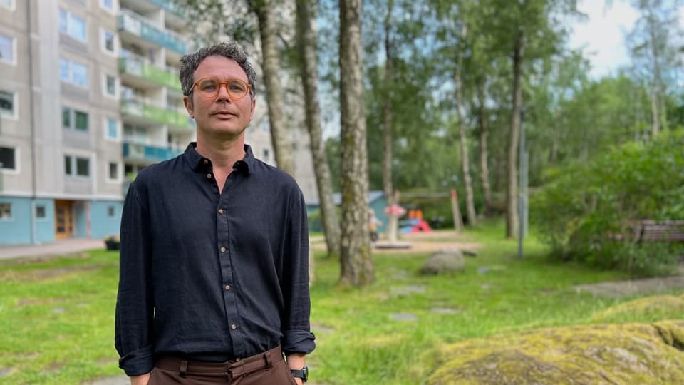 Foto av en man med kort hår, blå skjorta och glasögon