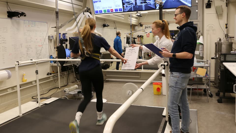 Labbmiljö med en löpare på band och forskare bredvid.