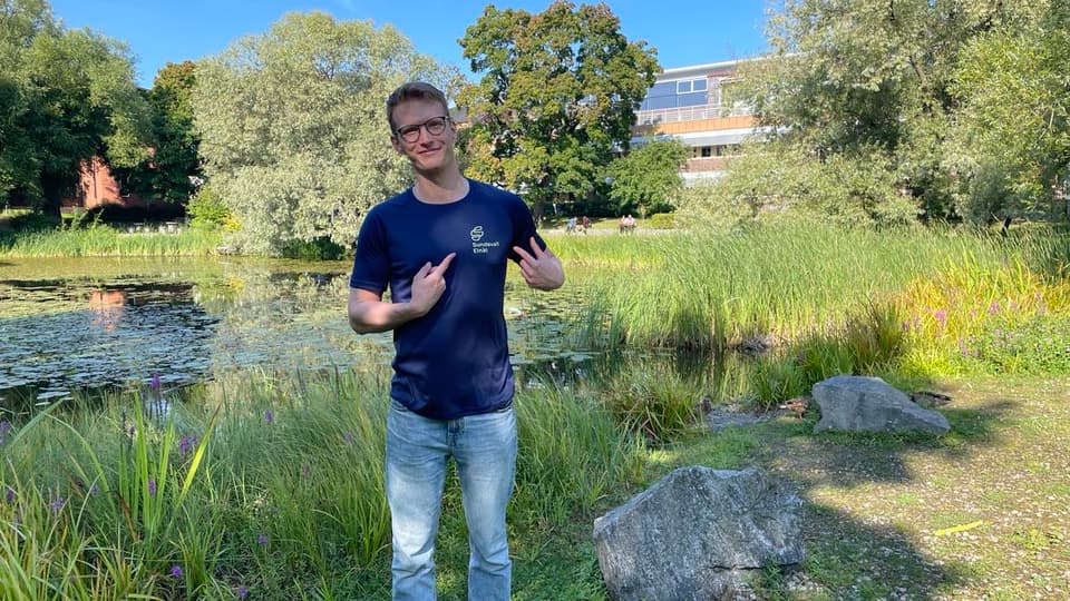 En man med blå tröja står vid vid en damm