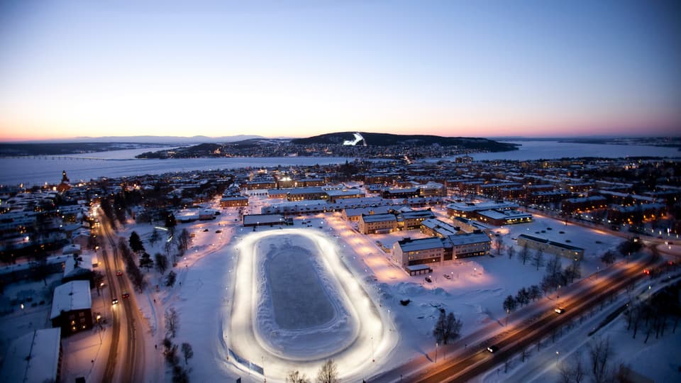 Fågelvy över en stadsbild med en sjö och fjäll i bakgrunden