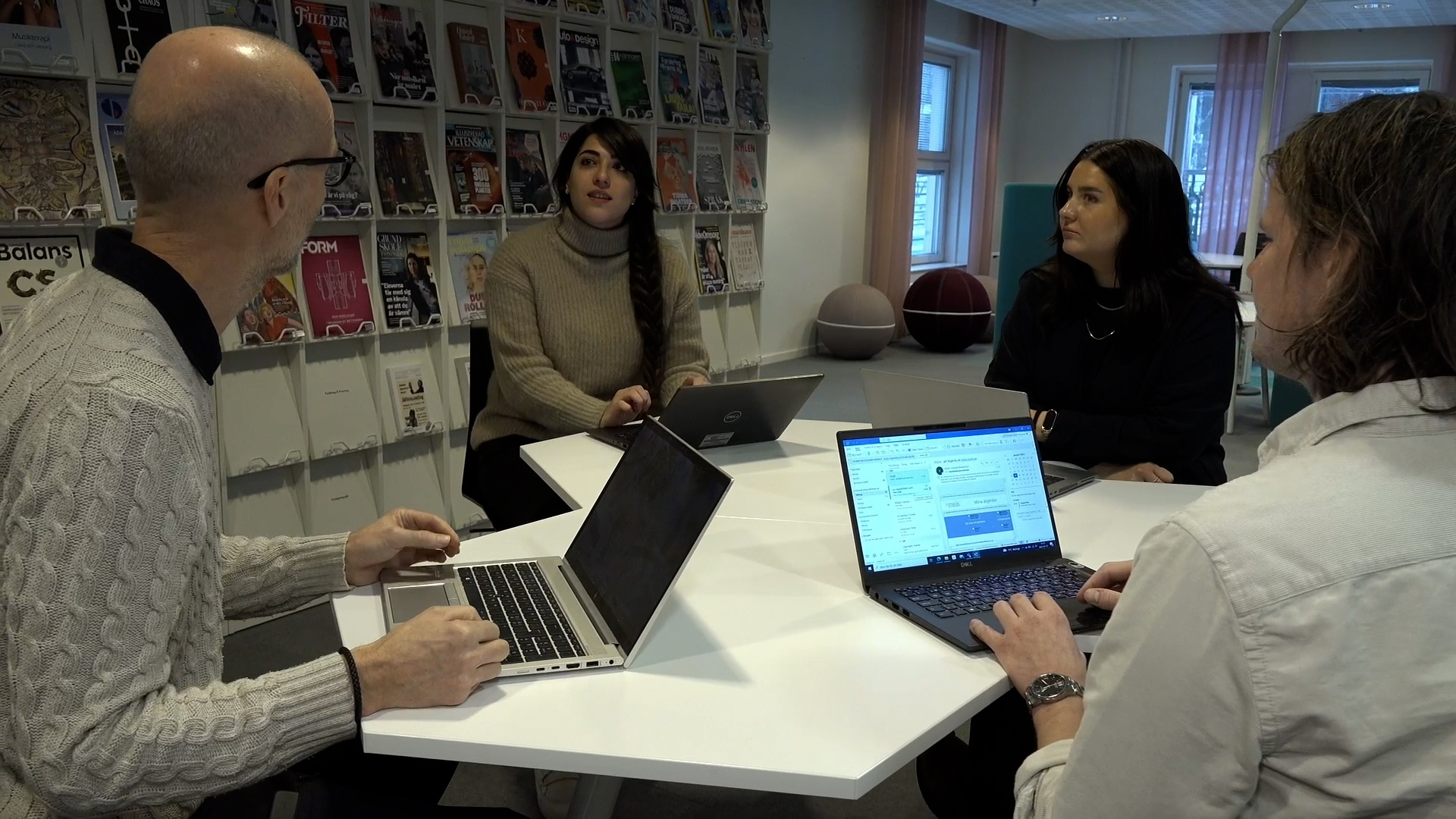 Fyra personer med varsin bärbar dator sitter vid ett bord och samtalar. 