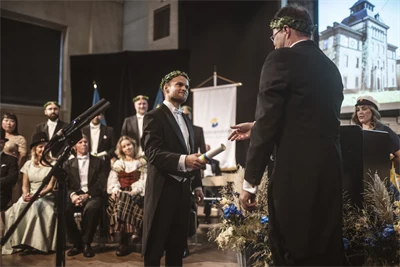Two well-dressed people wearing laurel wreaths are standing on a stage.