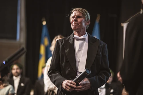 A well-dressed man is holding a professor's diploma.
