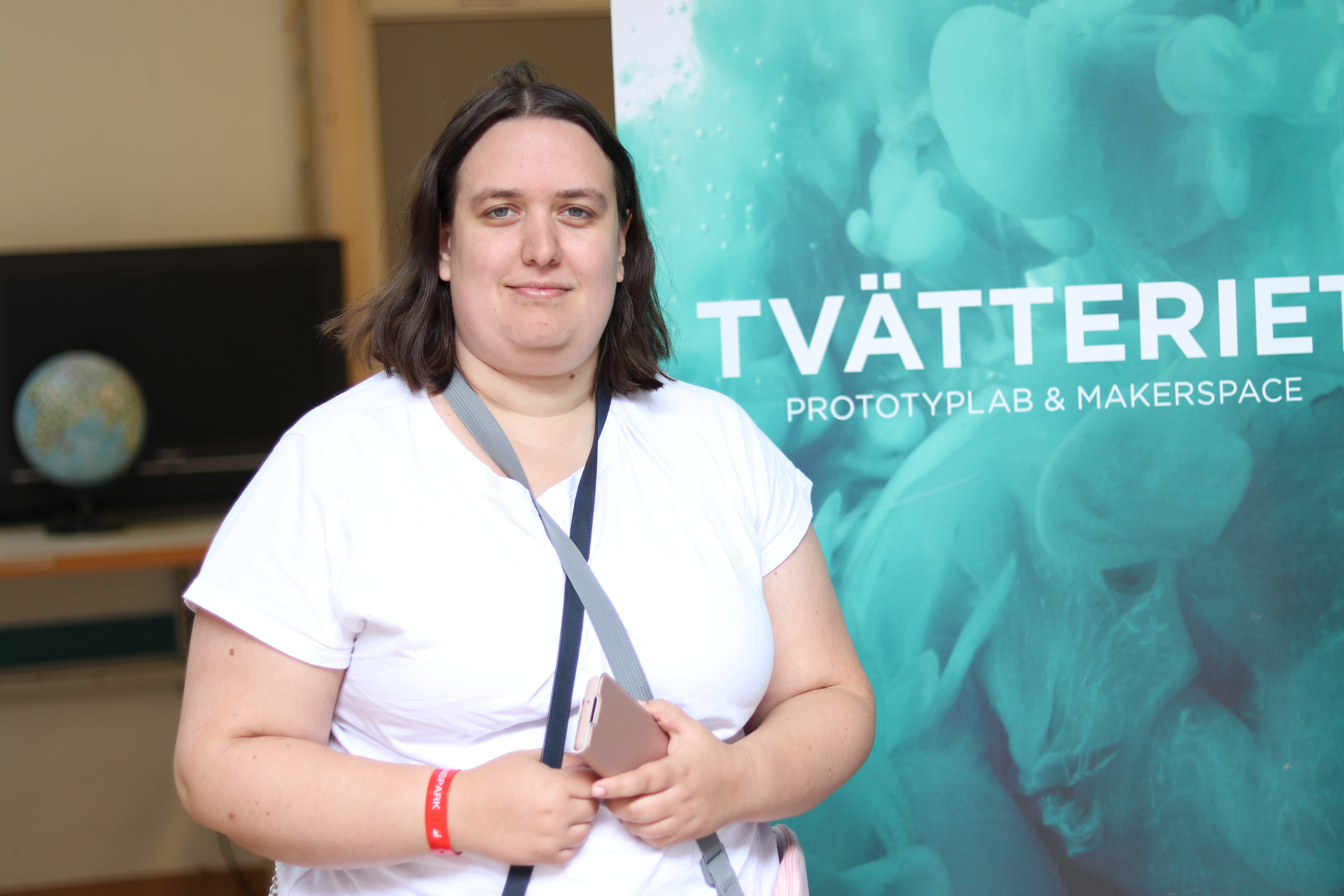 Kvinna i vit t-shirt står framför en blå rollup med texten 