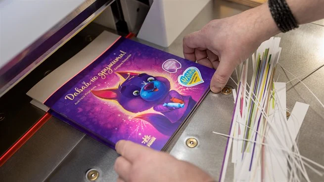 two hands holding a childrens book in a book cutter machine